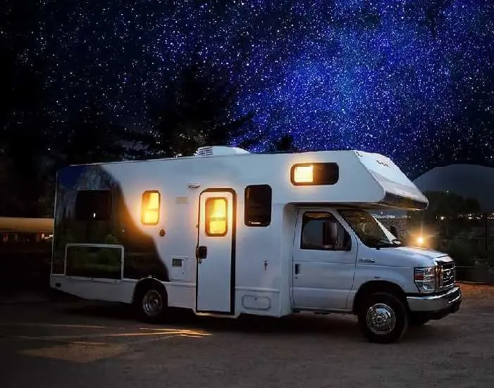 A white rv parked in the dark under a night sky.